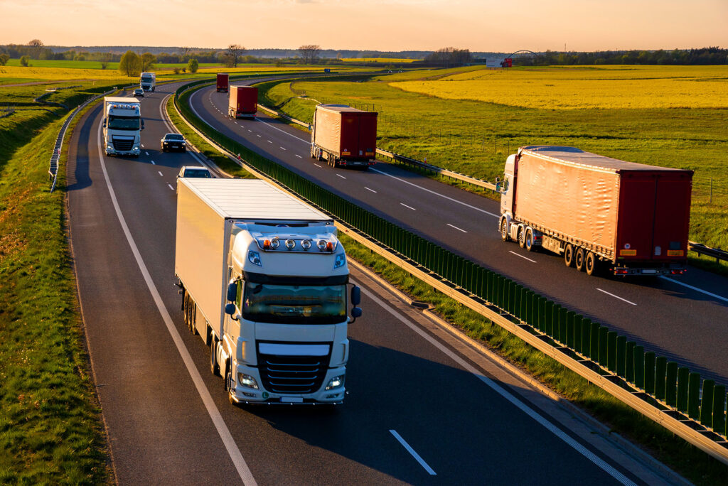 Convoy of semi trucks driving on highway at sunset
